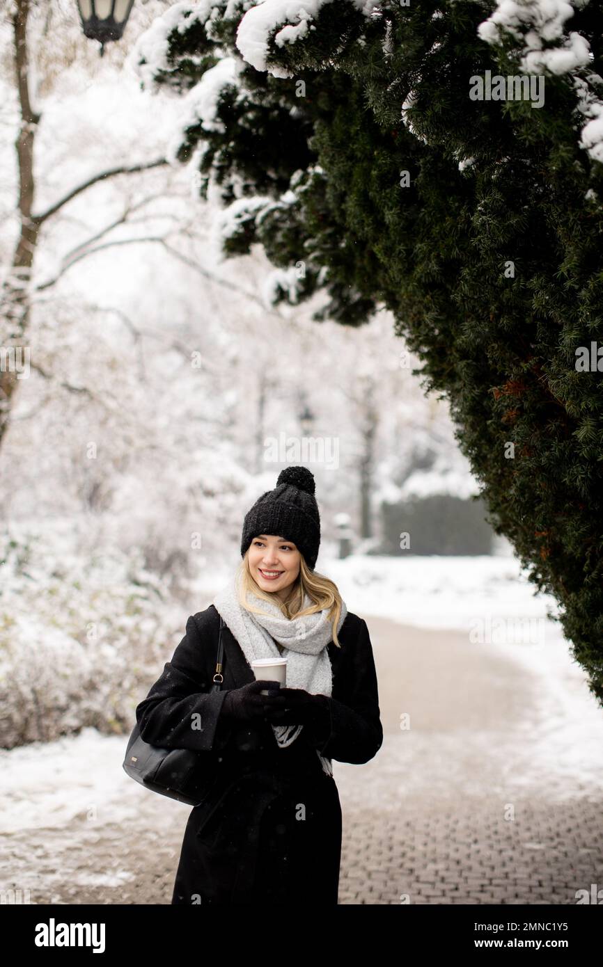 Pretty young woman n warm clothes enjoying in snow with takeaway coffee cup Stock Photo
