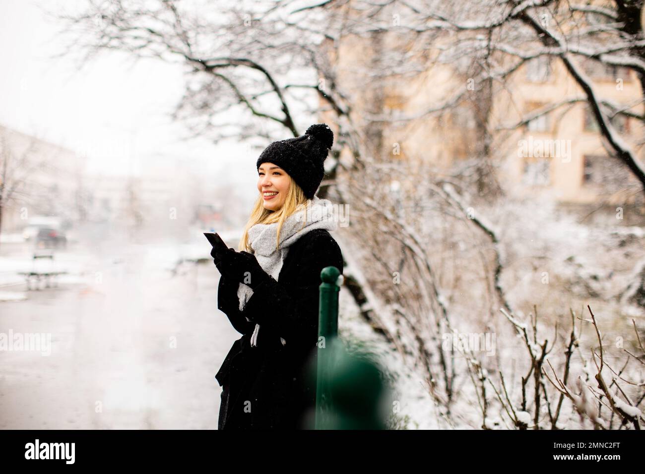 Pretty young woman n warm clothes enjoying in snow and using mobile phone Stock Photo