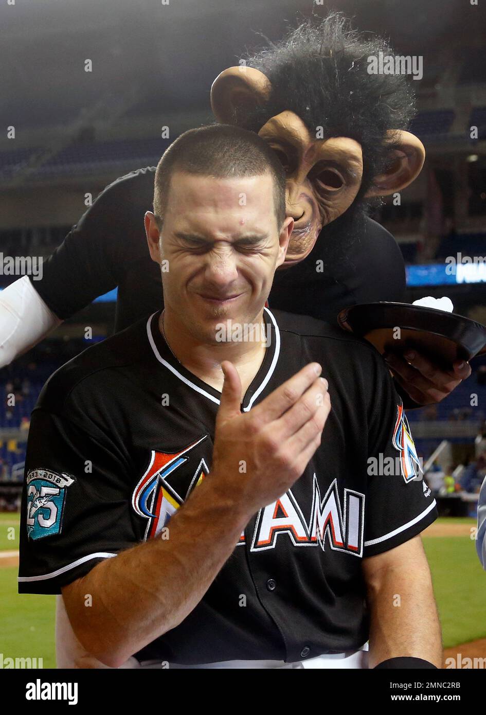 Wearing a monkey mask, Miami Marlins' Miguel Rojas, top, prepares to hit  J.T. Realmuto with a shaving cream pie as Realmuto does a postgame  interview after a baseball game against the Atlanta