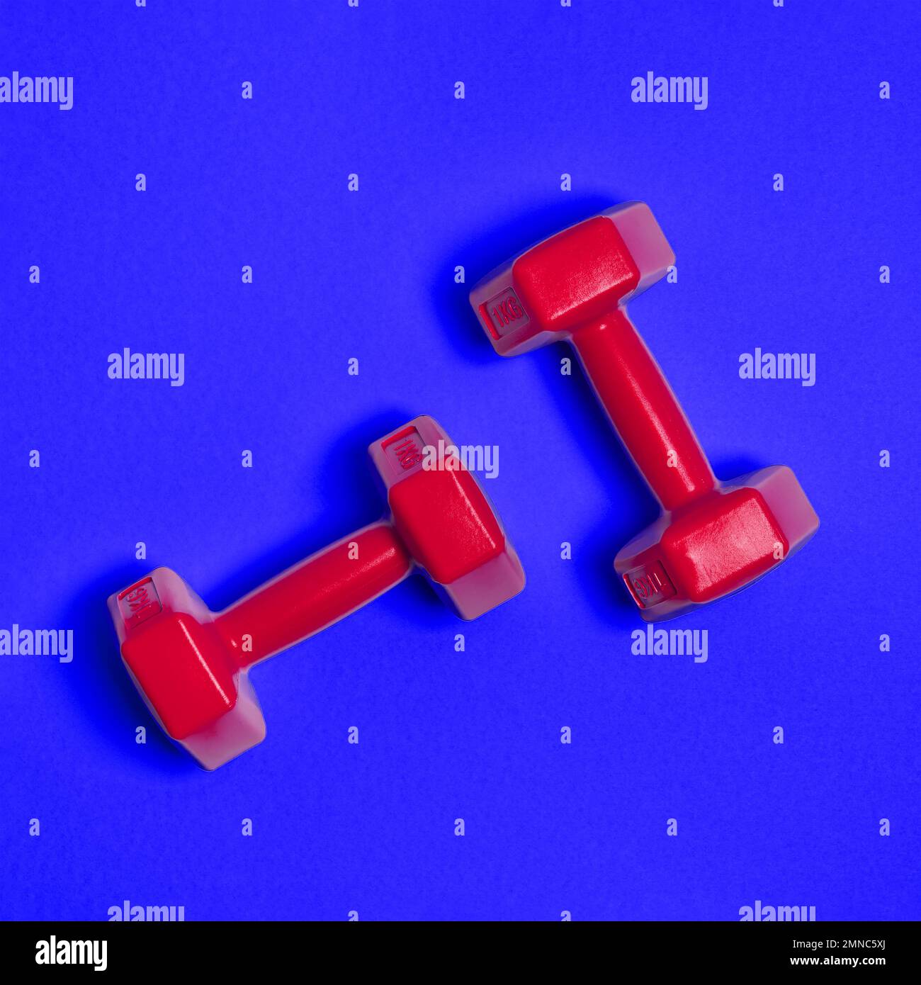 Two bright red dumbbells are isolated on blue background. Sport and health concept. Stock Photo