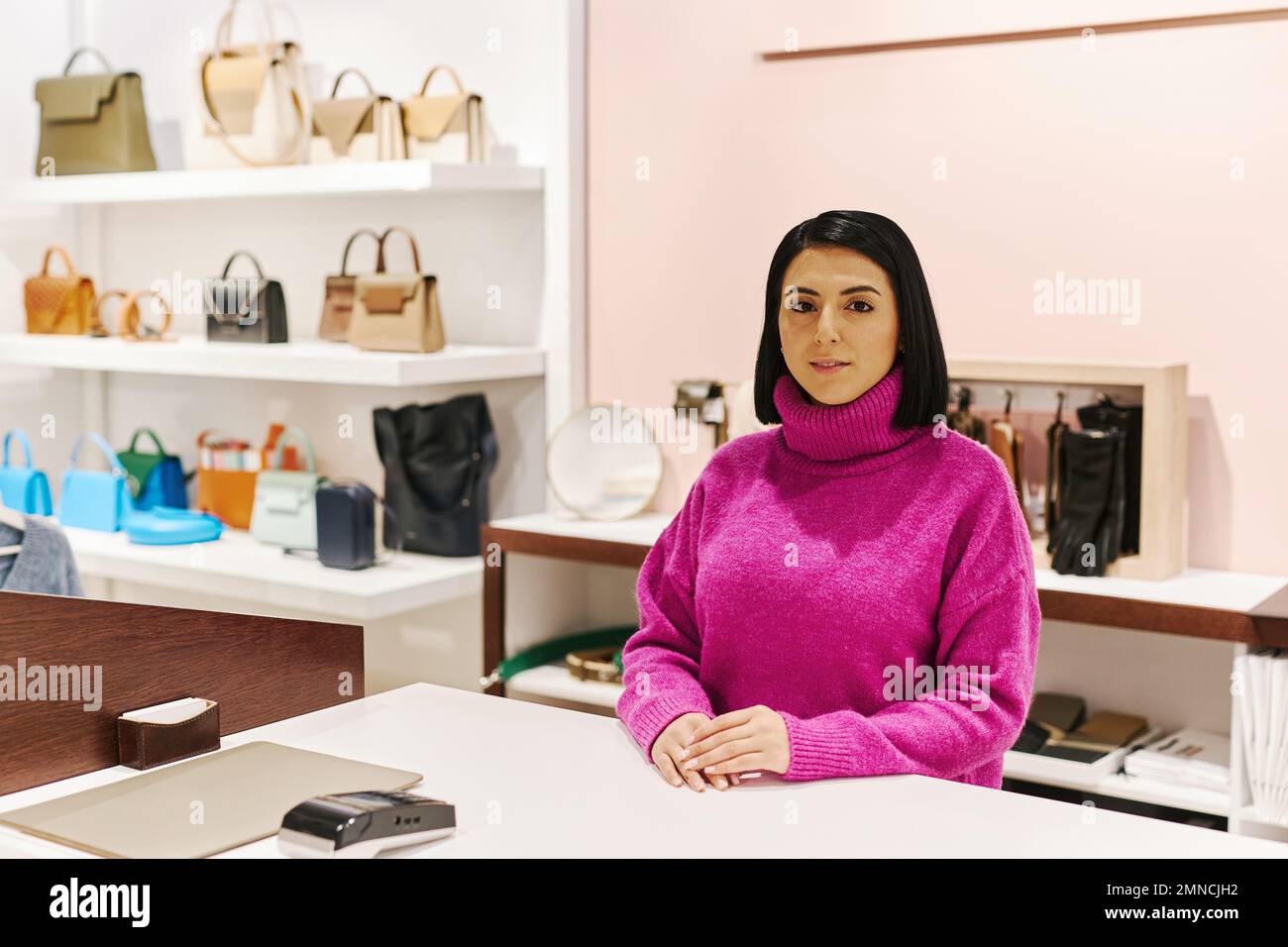 Waist up portrait of young woman working luxury clothing and accessories boutique and wearing magenta sweater, copy space Stock Photo