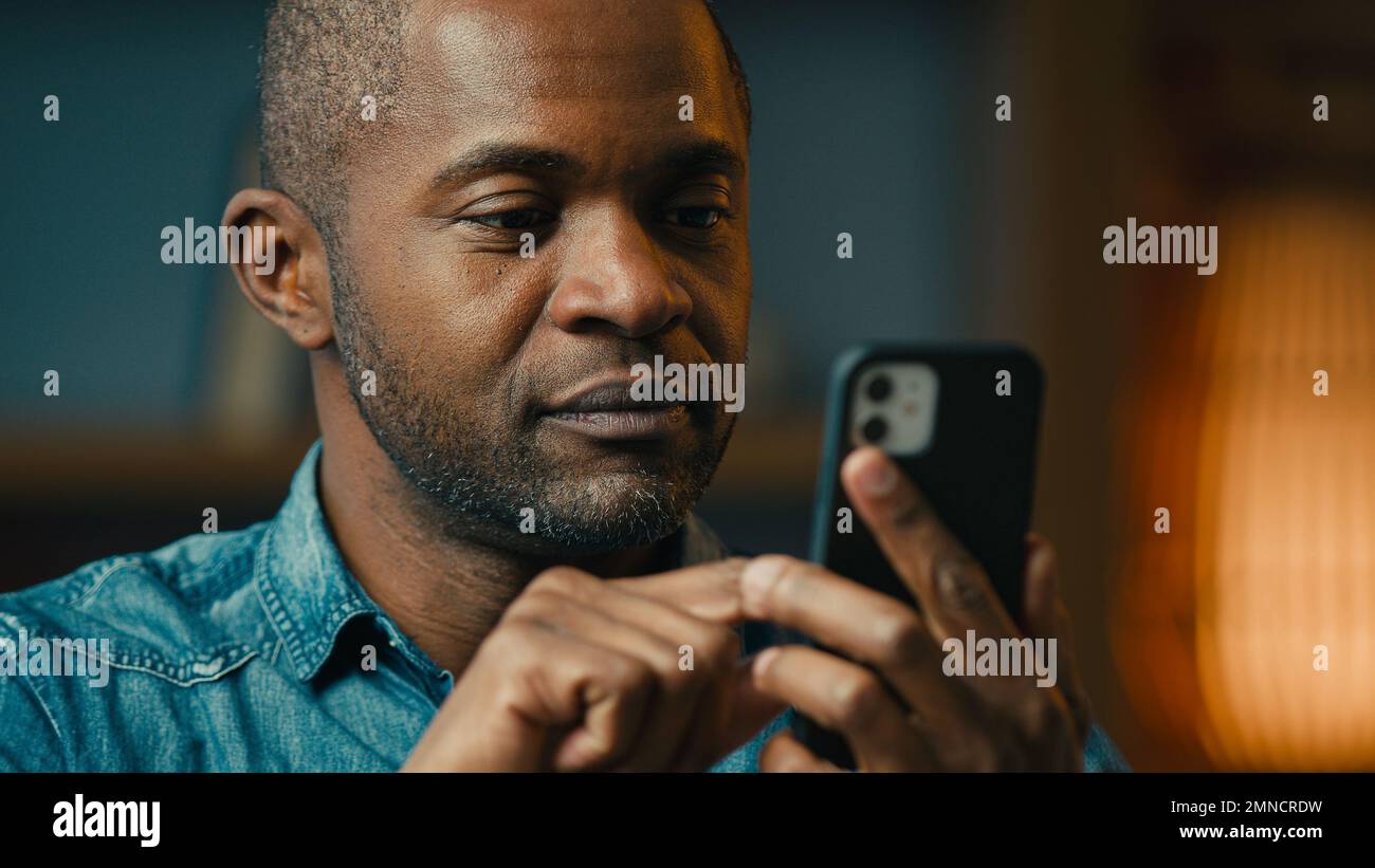 Close-up surprised mature african american man holding smartphone reading good news in Internet excited ethnic male winner win in mobile online Stock Photo