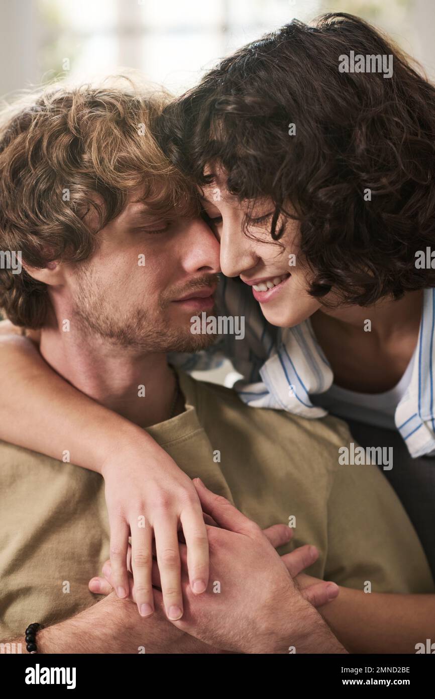 Close-up portrait of young affectionate couple expressing tenderness and love to one another while pretty woman embracing her husband Stock Photo