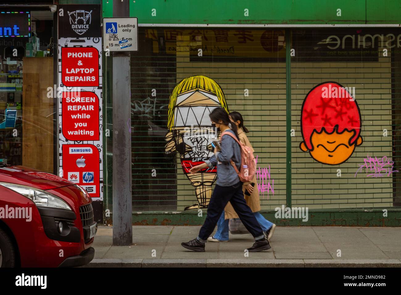 Asian couple walking in the street in front of a closed shop store with graffiti in Liverpool, United Kingdom Stock Photo