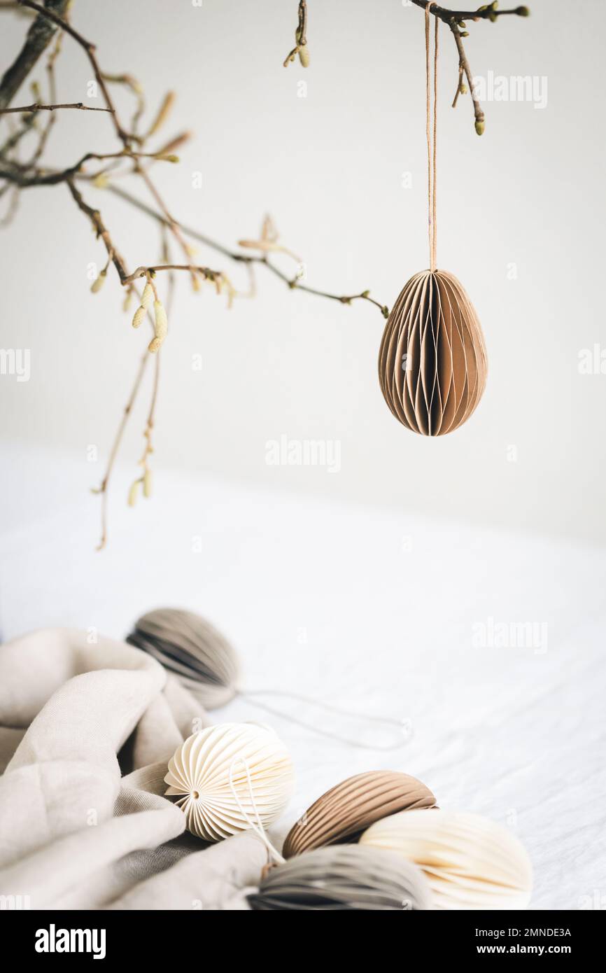 Easter paper egg hanging on branch under table with decorations. Stock Photo