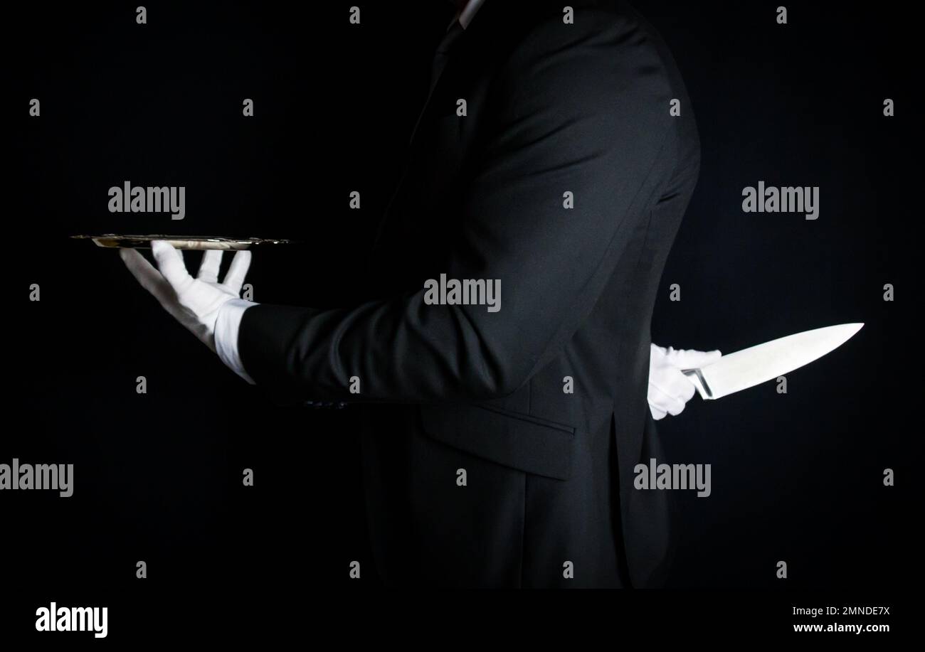 Butler in Dark Suit and White Gloves With Serving Tray and Holding Knife Behind His Back. Concept of Butler Did It. Stock Photo