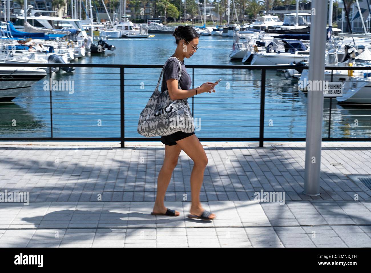 A woman looks at her phone while walking in Marina Del Rey, California, USA. Stock Photo