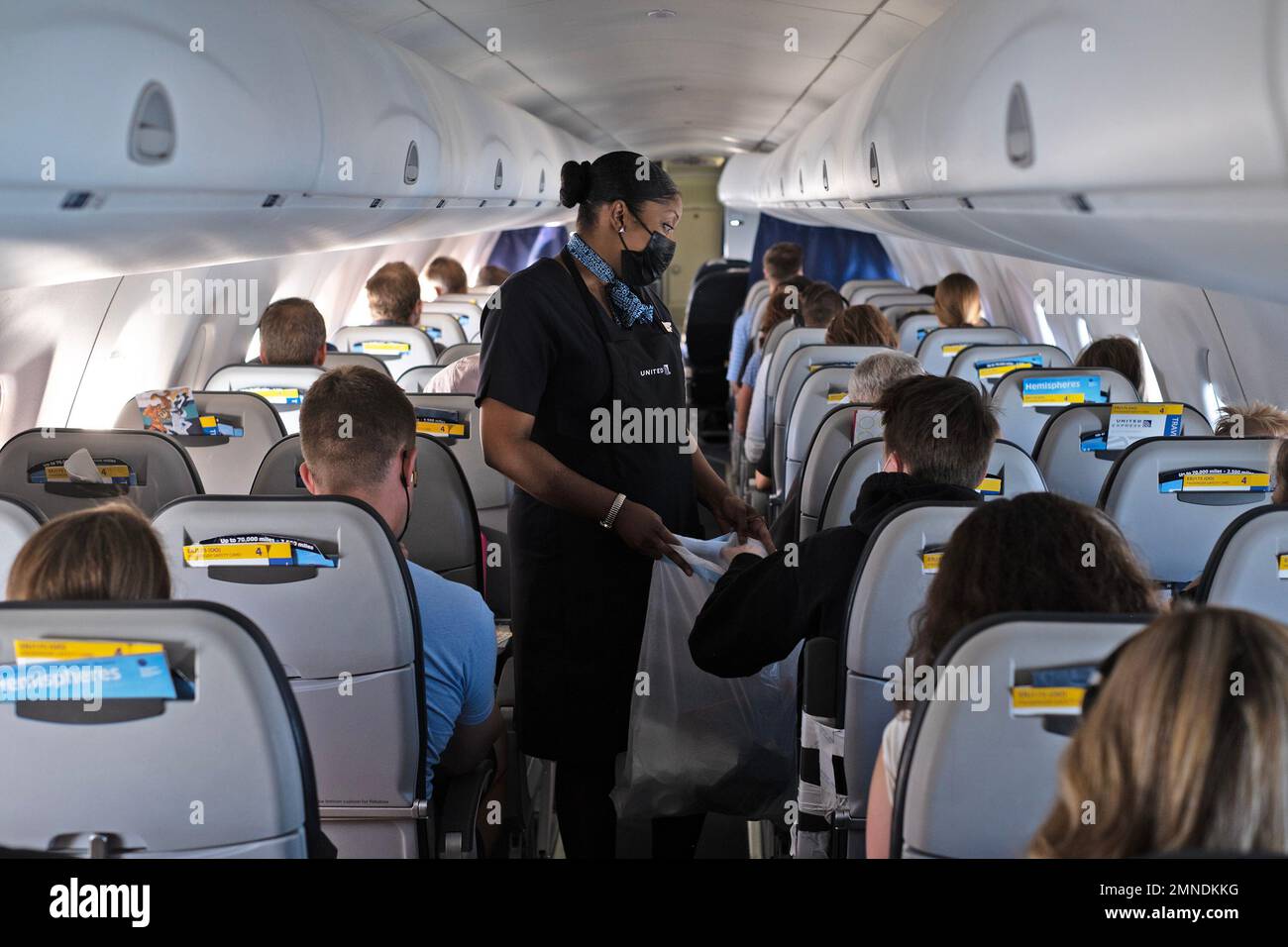 A flight attendant collects trash from passengers. Stock Photo
