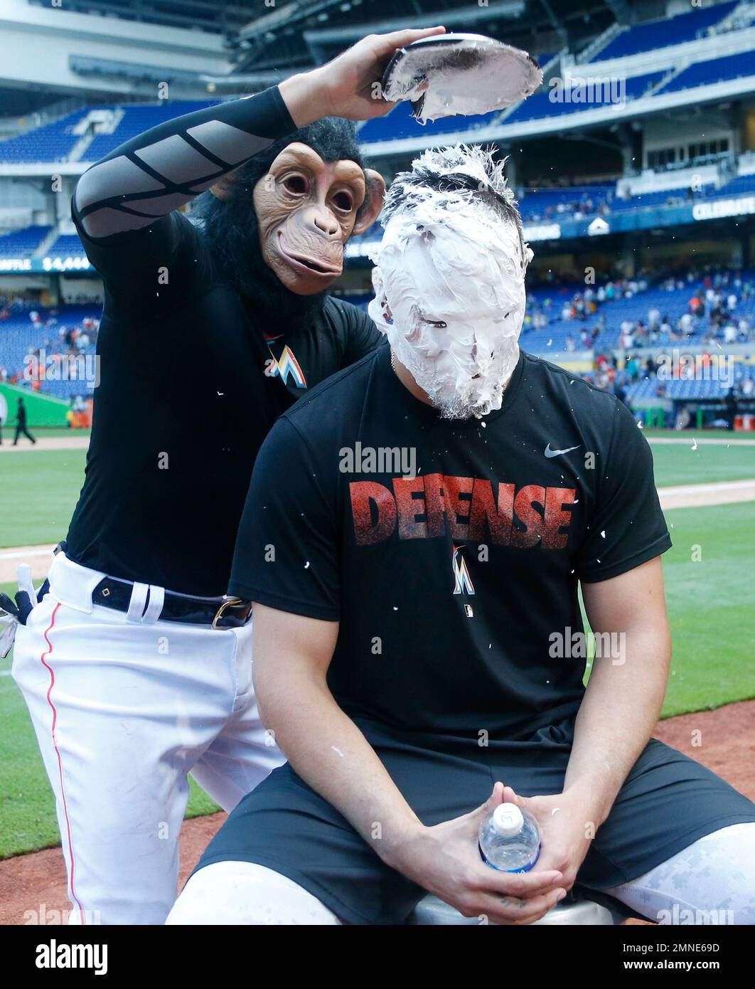 Wearing a monkey mask, Miami Marlins' Miguel Rojas, top, prepares to hit  J.T. Realmuto with a shaving cream pie as Realmuto does a postgame  interview after a baseball game against the Atlanta