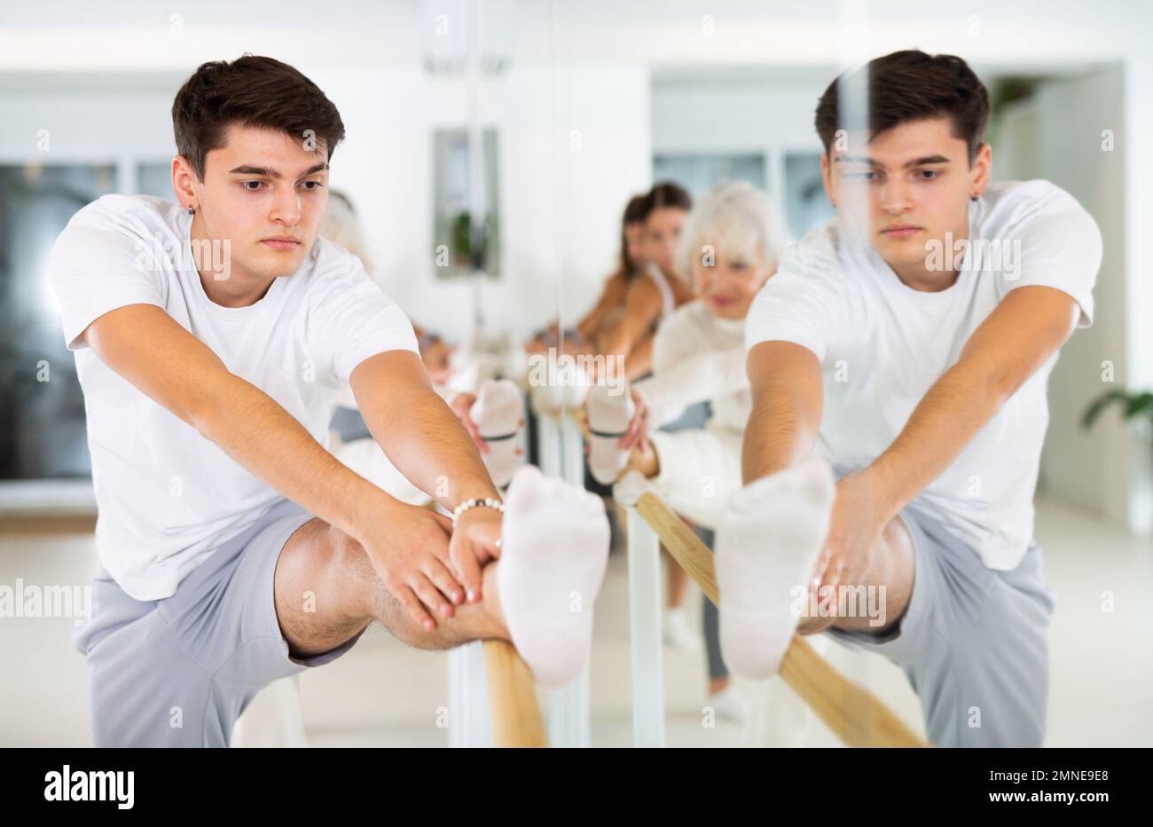 Dancer man exercise stretching on a ballet barre at a group training session in the dance studio
