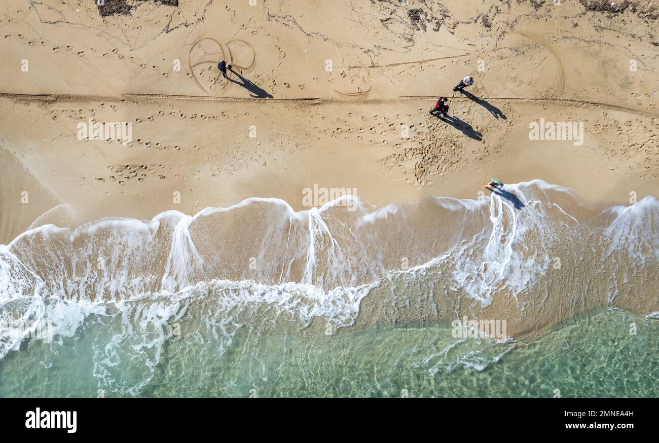 Drone aerial scenery of unrecognised people walking in a sandy beach in winter. Windy waves crashing on the shore. Protaras Cyprus Stock Photo