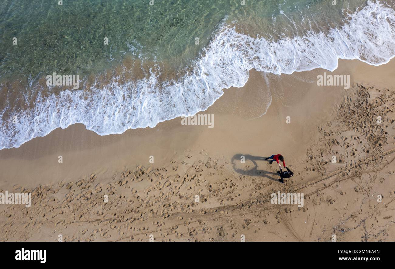 Drone aerial scenery of unrecognised people walking in a sandy beach in winter. Windy waves crashing on the shore. Protaras Cyprus Stock Photo