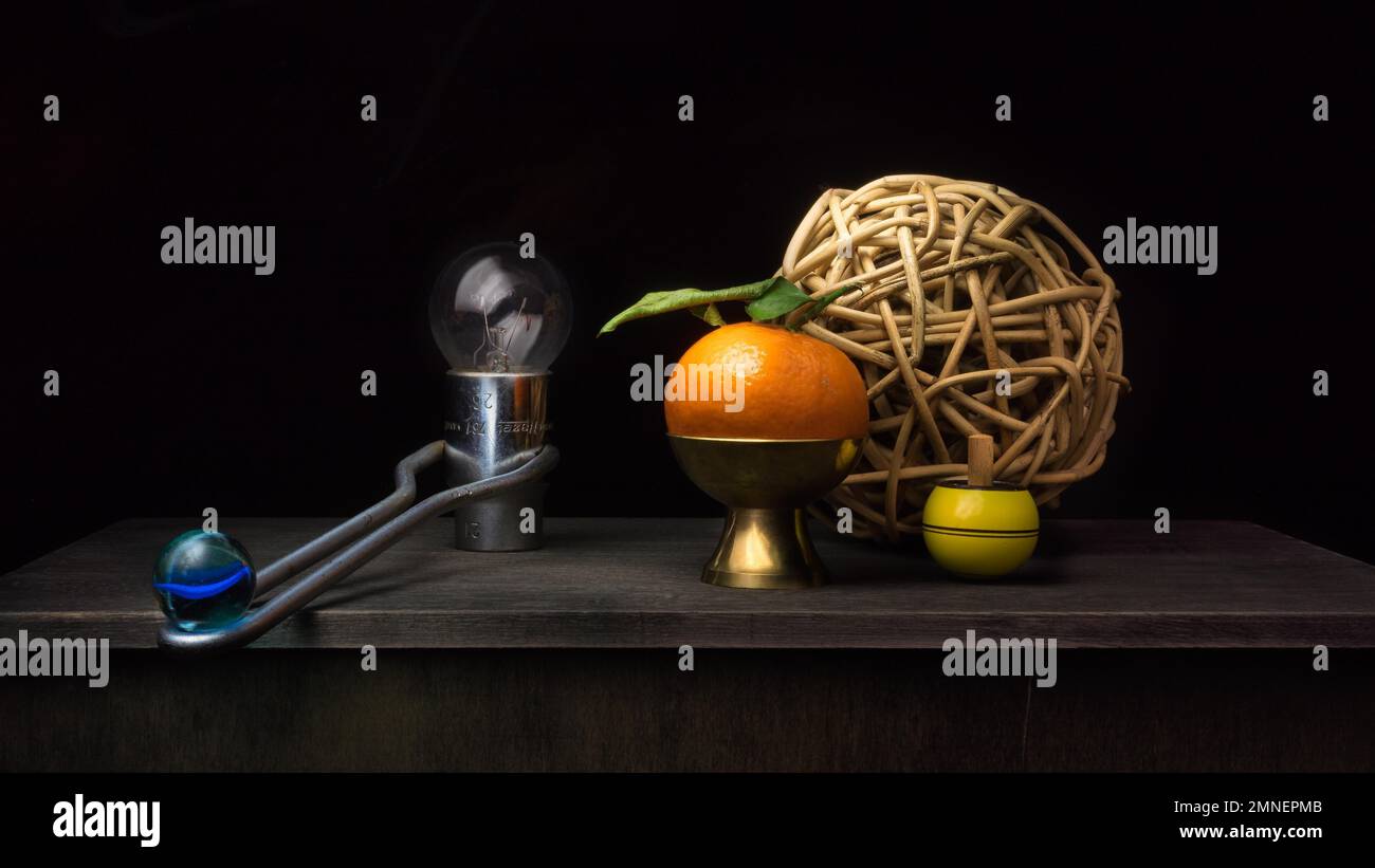 Still life with tangerine, wooden balls, glass ball and light bulb in socket spanner, studio shot, dark background Stock Photo