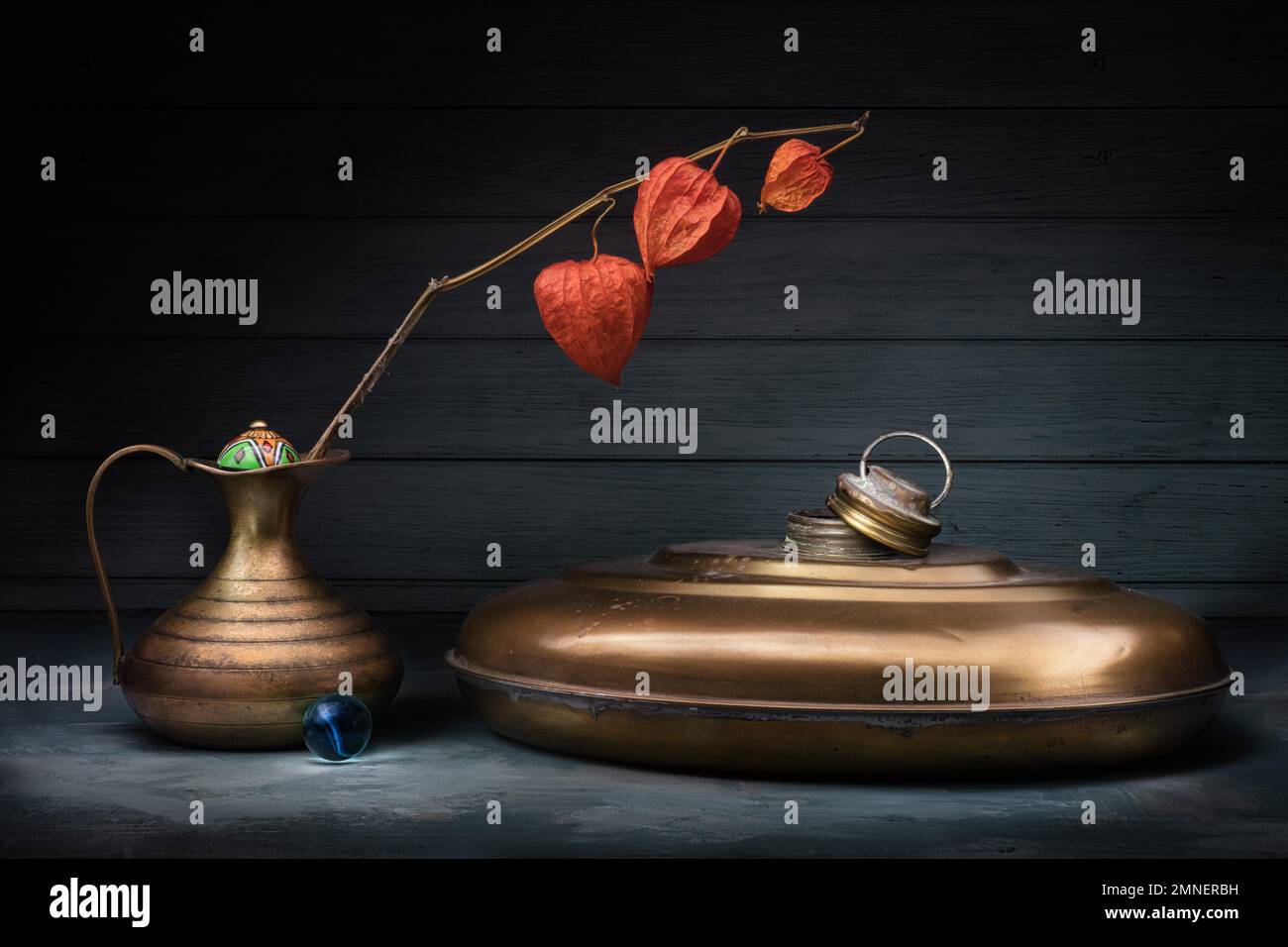 Still life with physalis in copper vase, old hotwater bottle and glass