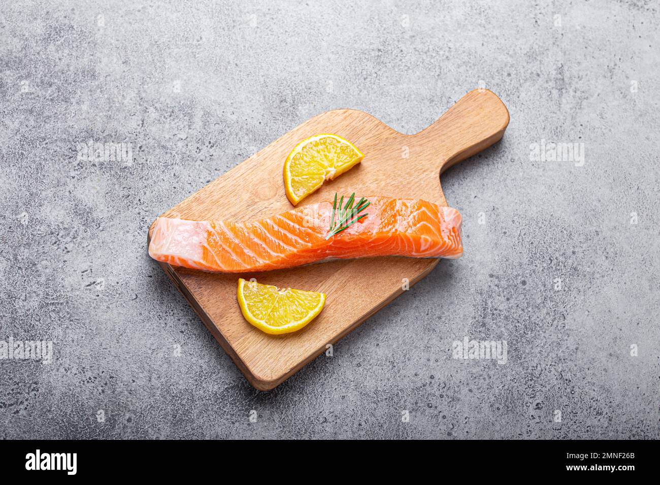 Raw salmon fish fillet with lemon wedges and rosemary on wooden cutting ...