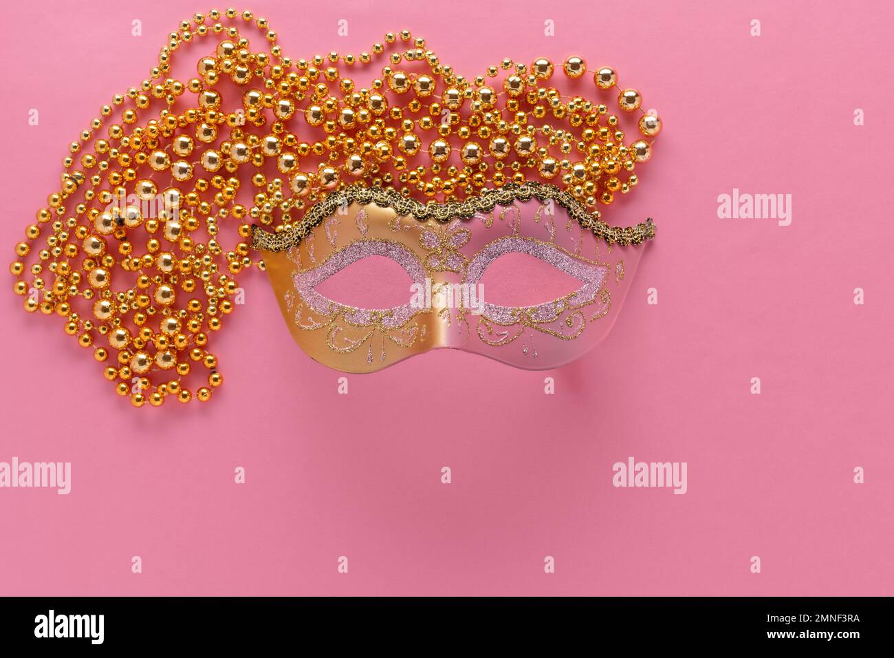 mardi gras or carnival theme with pink and gold mask and gold beads on pink background Stock Photo