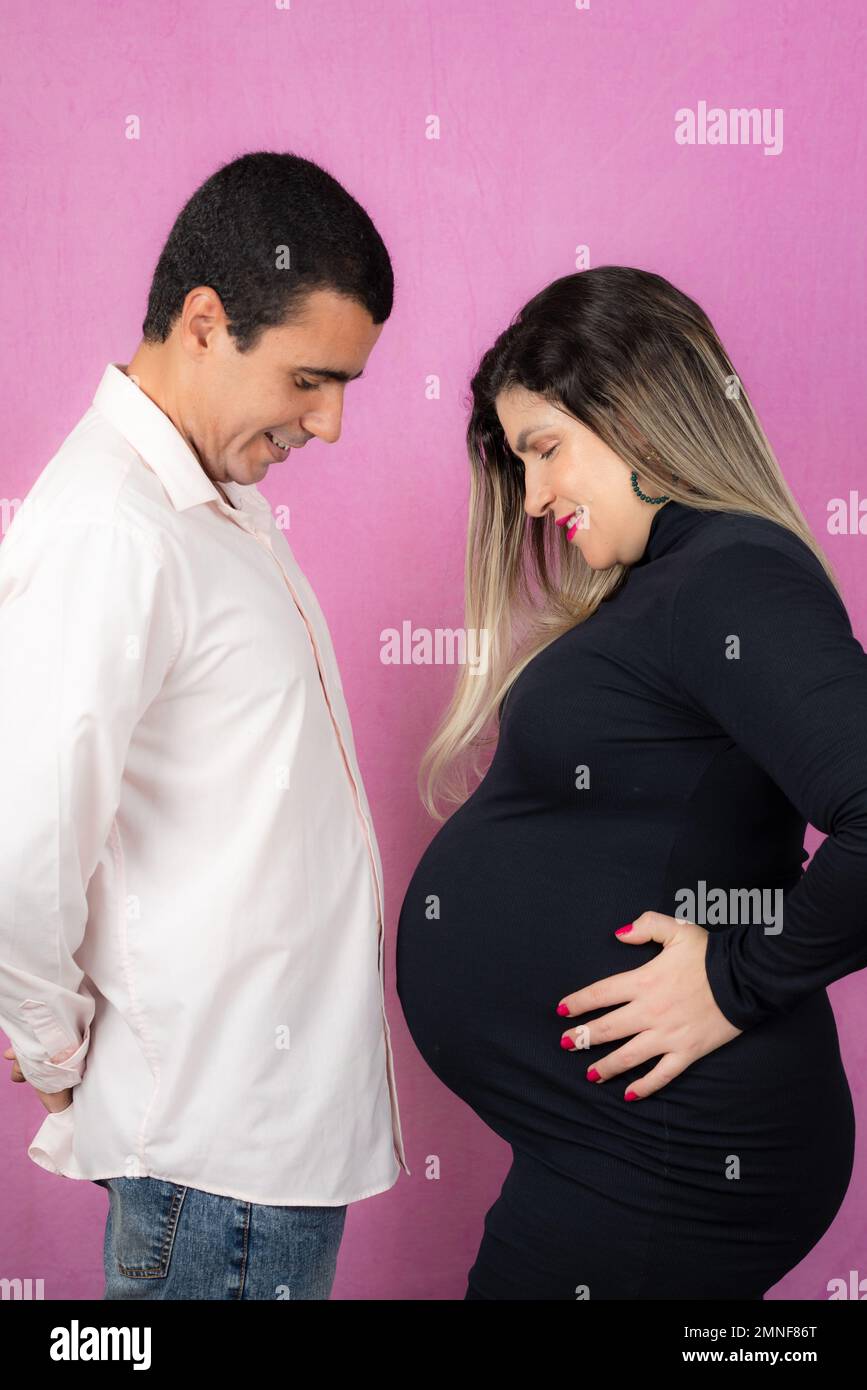 Man posing with his pregnant wife. Isolated on pink background. Stock Photo