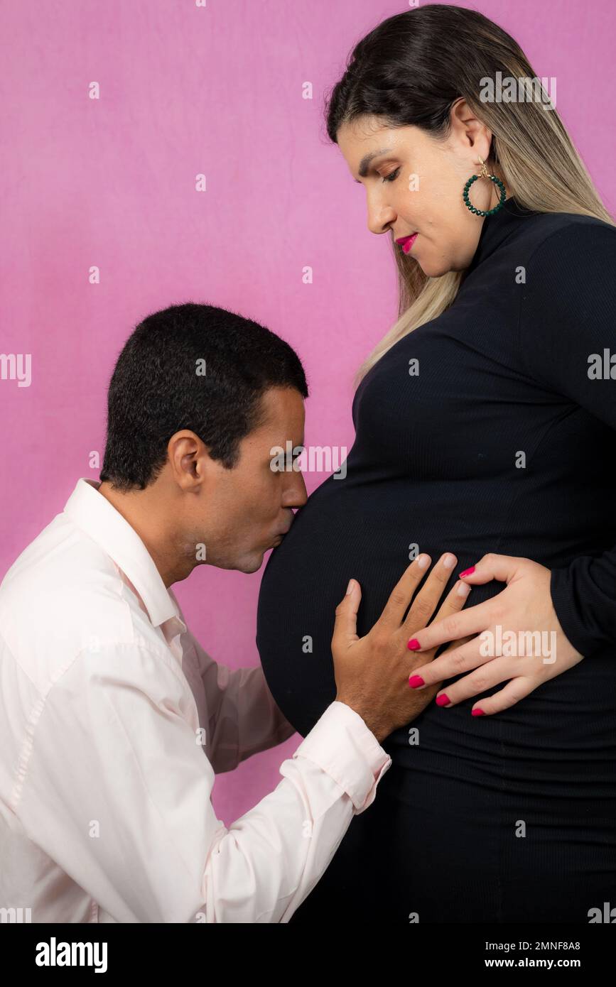 Husband kissing wife's belly. Isolated on pink background. Stock Photo