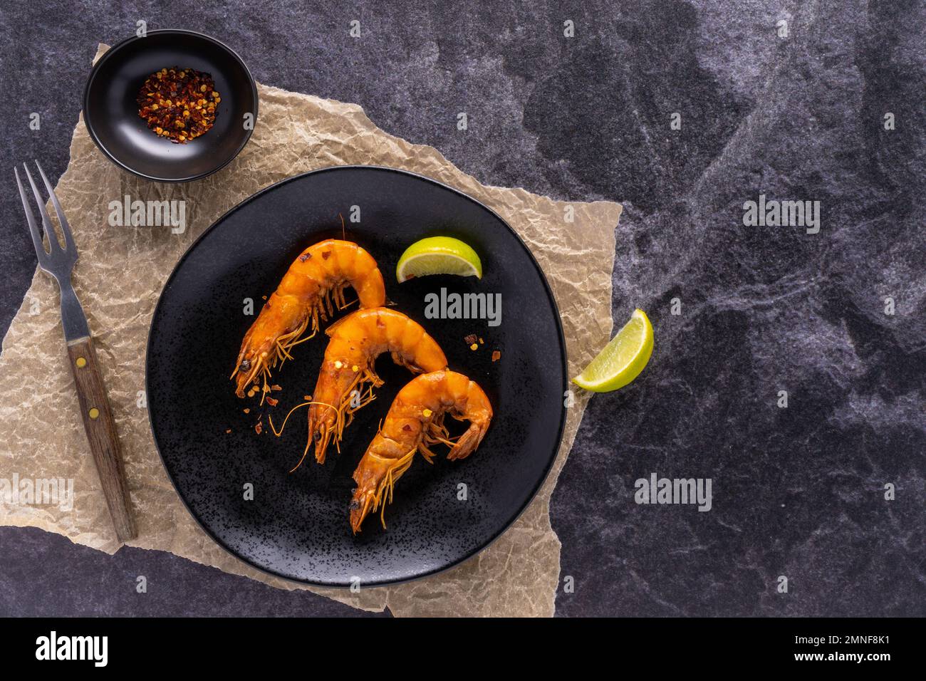 chili lime shrimp with heads on a black plate marble counter with wood handle fork Stock Photo
