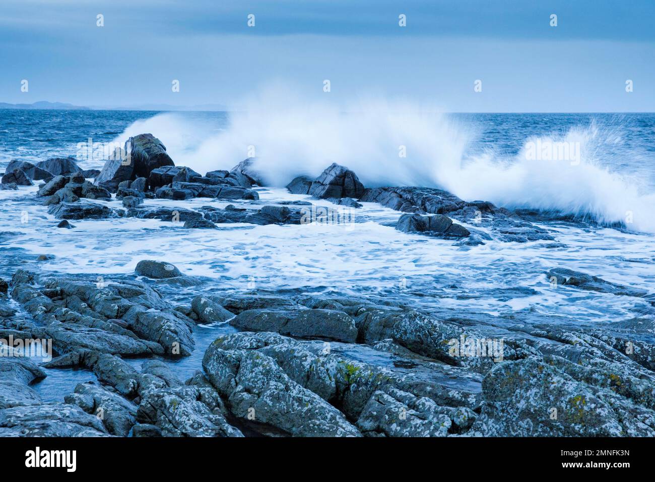 Stormy sea dashes against rocks at dawn in the blue hour, at Reiff on the west coast of Scotland Stock Photo