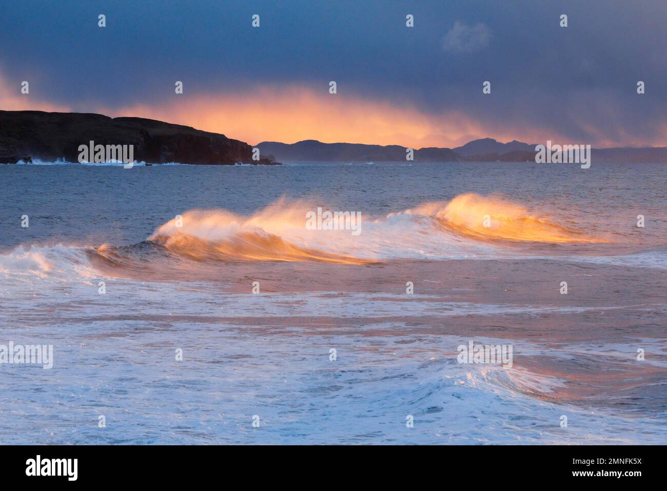 Large waves crash in a winter storm and the swirling spray is illuminated by the warm light of the evening sun, Summer Isles in the background, at Stock Photo