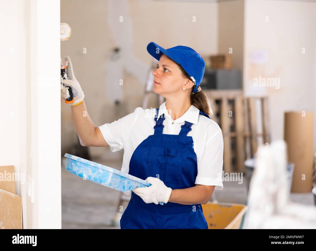 Professional female painter in blue overalls paints the walls with