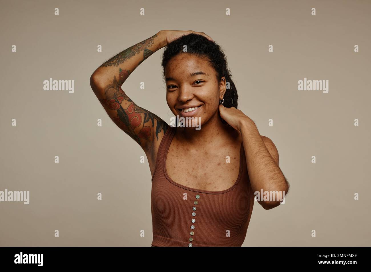 Candid portrait of ethnic young woman with tattoos looking at camera against neutral beige background, copy space Stock Photo