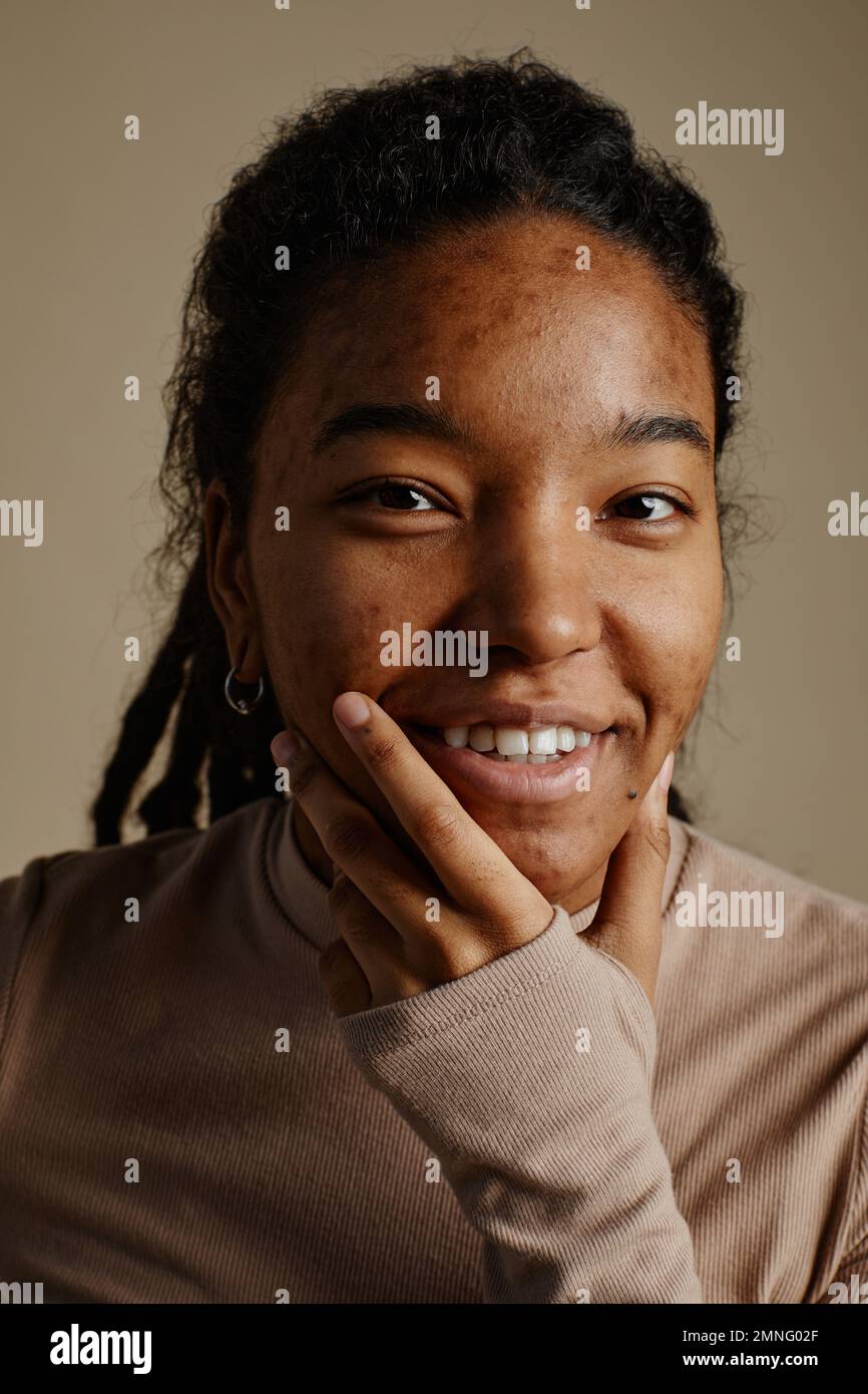 Close up portrait of young black woman smiling genuinely and looking at camera in neutral tones Stock Photo