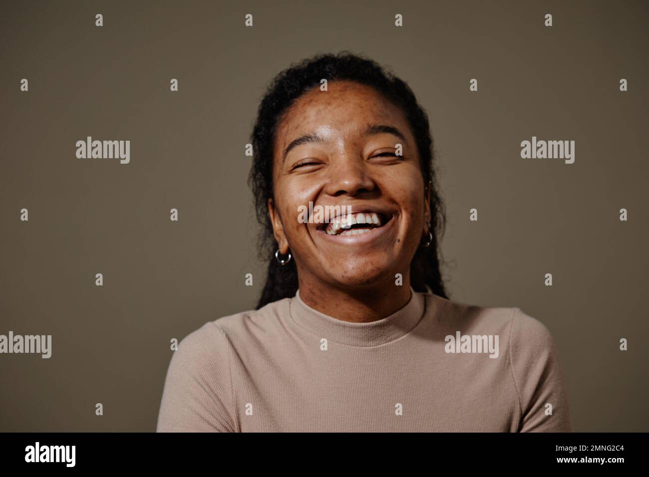 Candid portrait of black young woman laughing against neutral beige background in studio focus on skin texture Stock Photo
