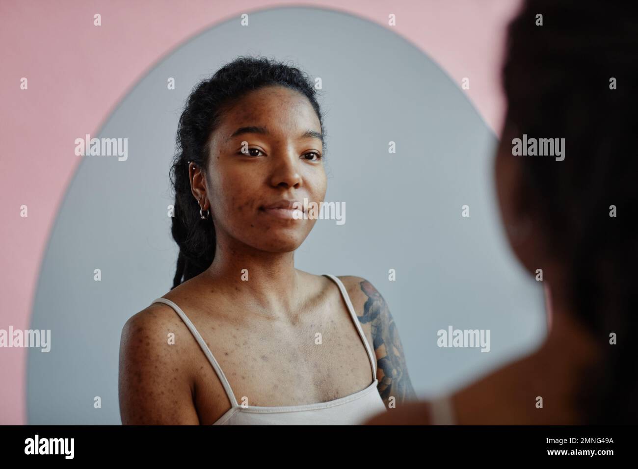 Young black woman with tattoos and acne scars looking in mirror smiling Stock Photo