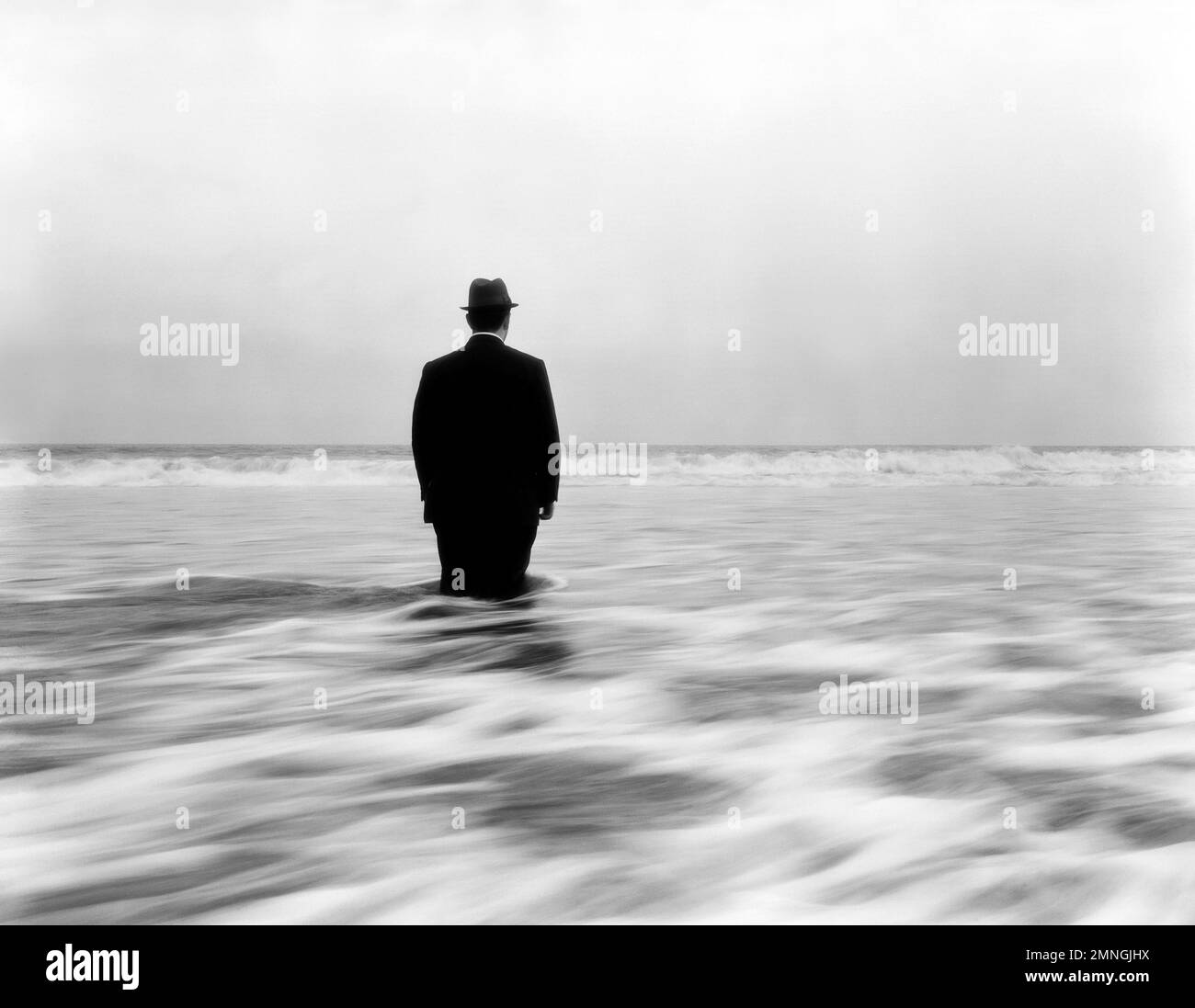 Rear View of Mid-Adult Man in Suit and Hat standing Knee-Deep in Ocean Water Stock Photo