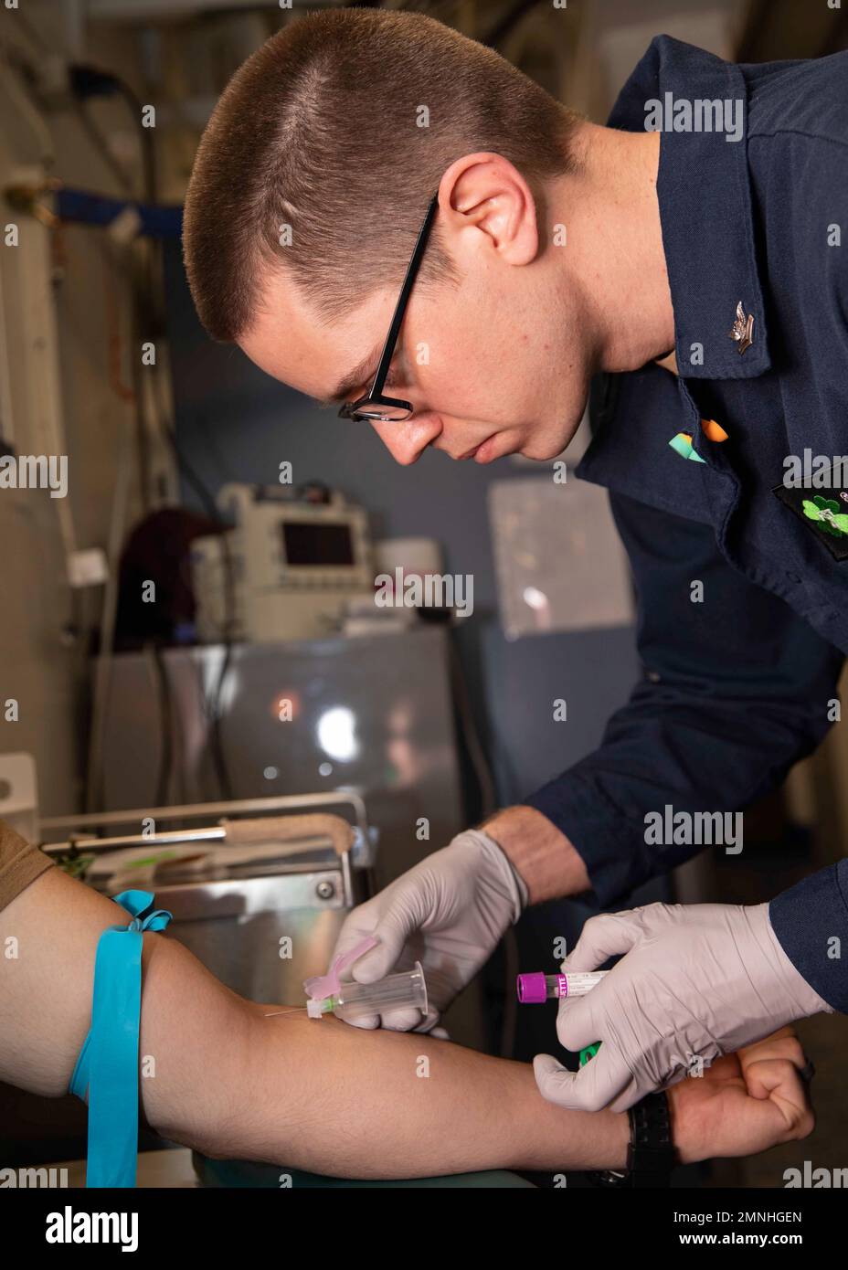 A hospital Corpsman 2nd Class, assigned to the Fleet Surgical Team (FST) 4, takes blood from a patient in the ship's medical department (USS Bataan) ca. 2020 Stock Photo