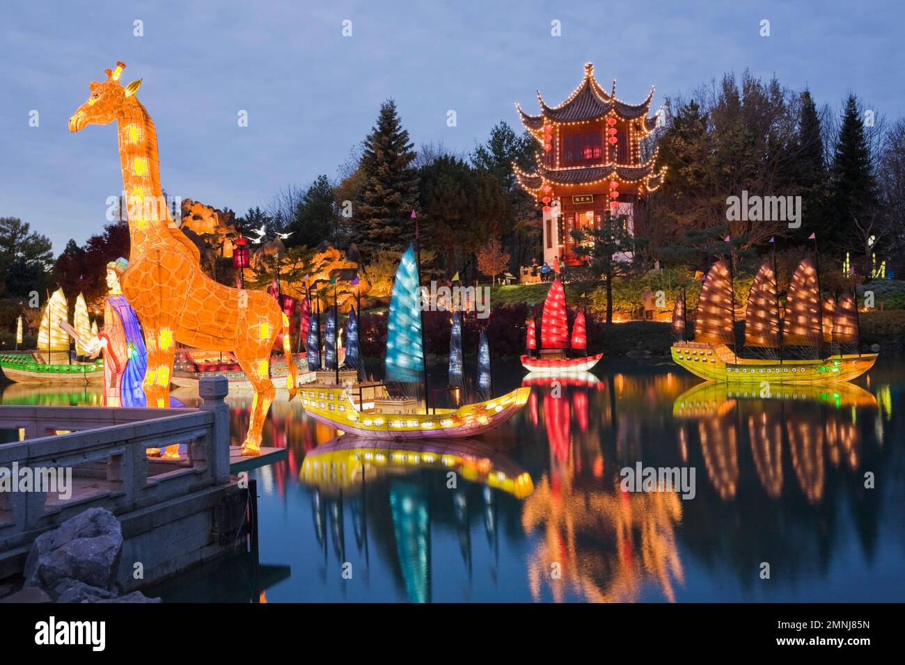 Illuminated giraffe and Chinese Junks lanterns on Dream Lake with Stone Mountain and Tower of Condensing Clouds pavilion in Chinese garden at dusk. Stock Photo