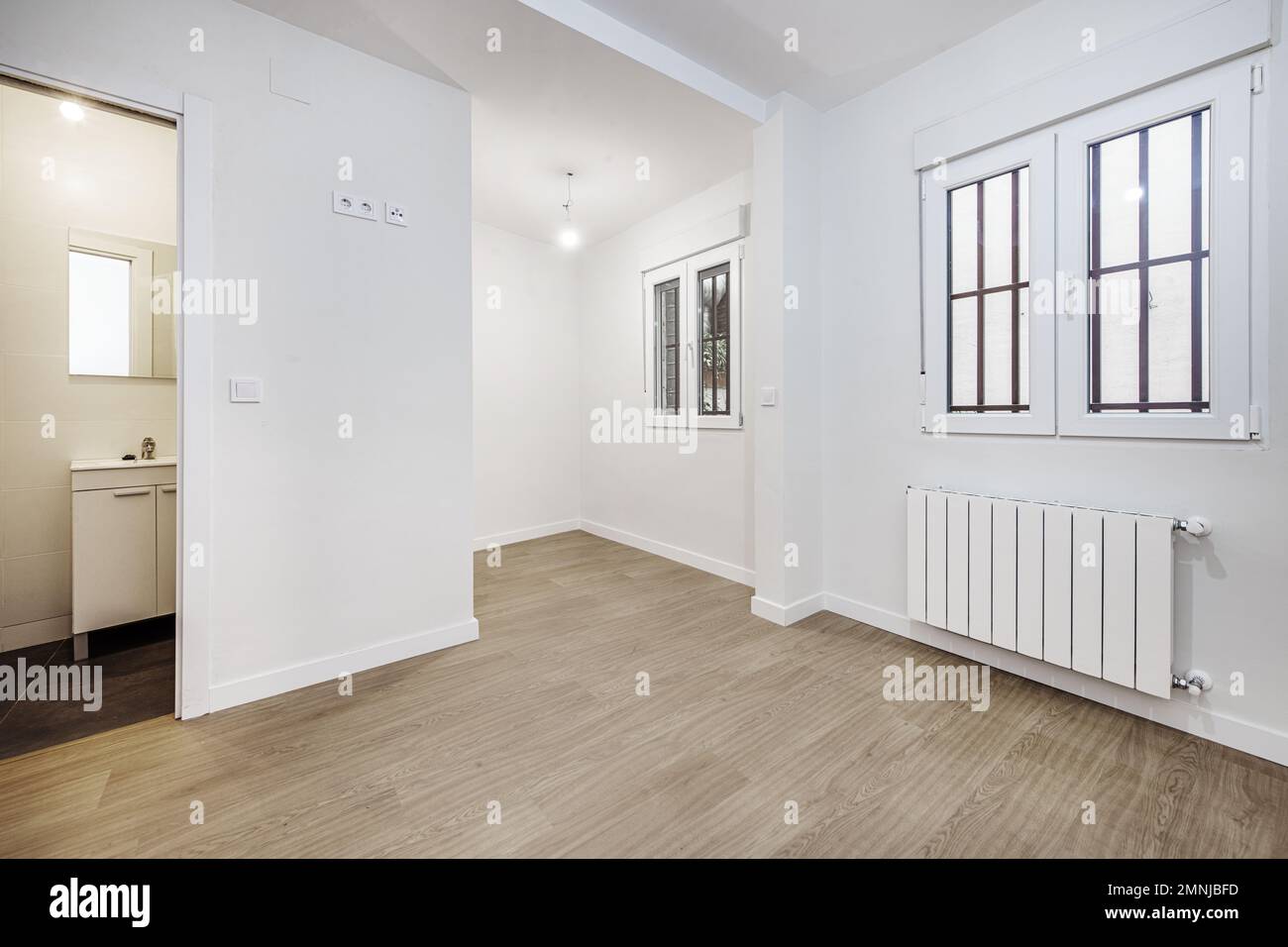 Empty room with laminate flooring, access to an en-suite bathroom and white aluminum windows with bars Stock Photo