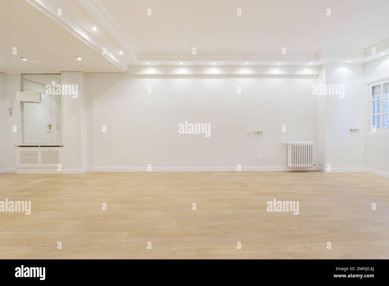 Empty living room with newly laid light hardwood floors, a mirrored sideboard and a white painted cast iron radiator Stock Photo