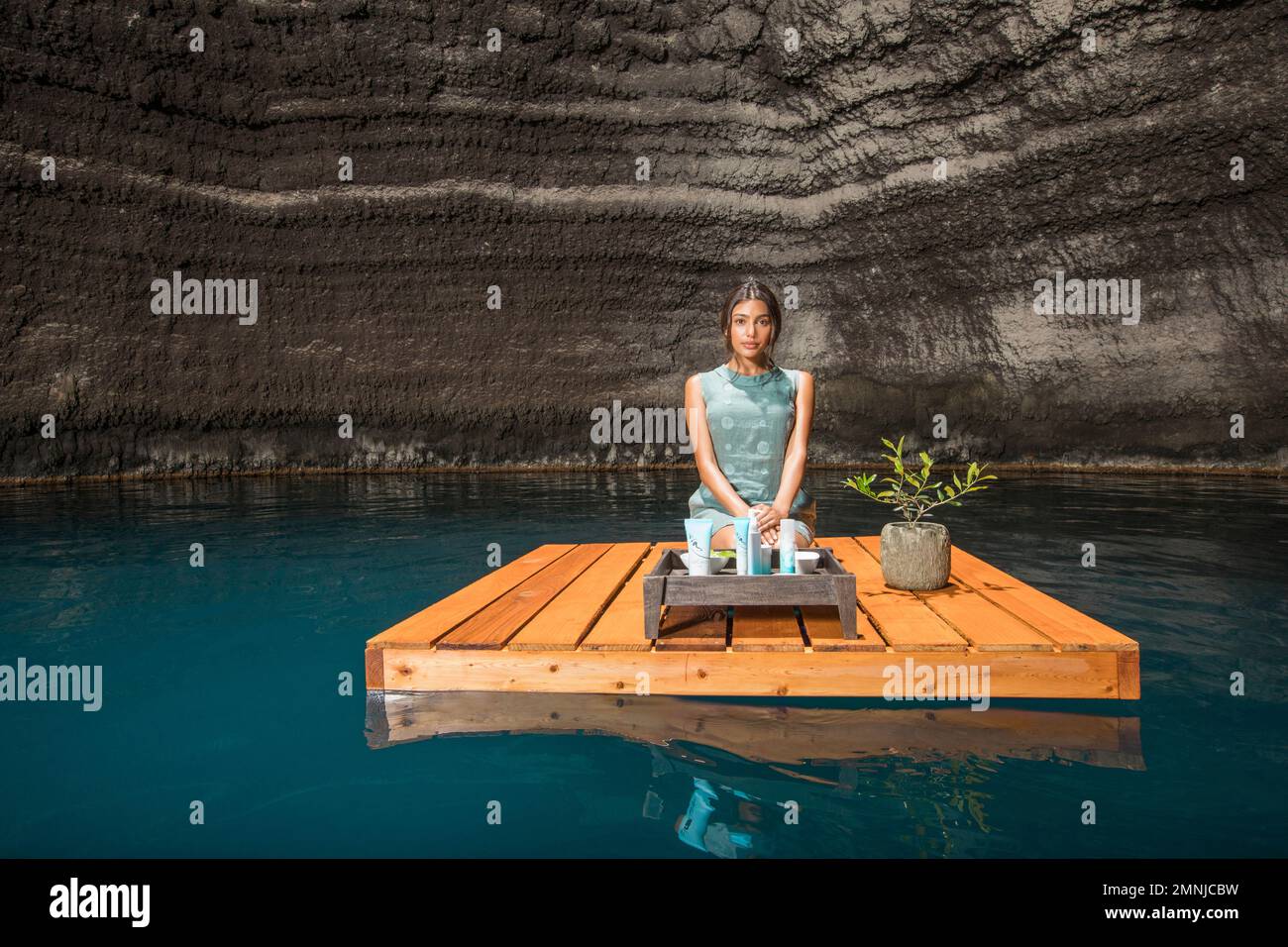 Beautiful woman kneeling on wooden raft on pond Stock Photo