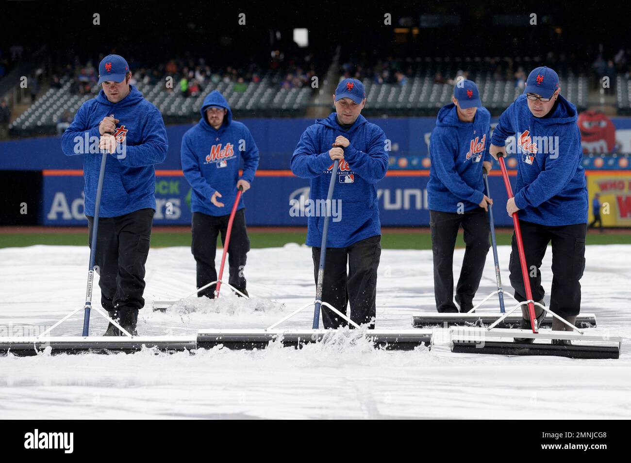 New York Mets employees push water off the rain tarp during a weather ...