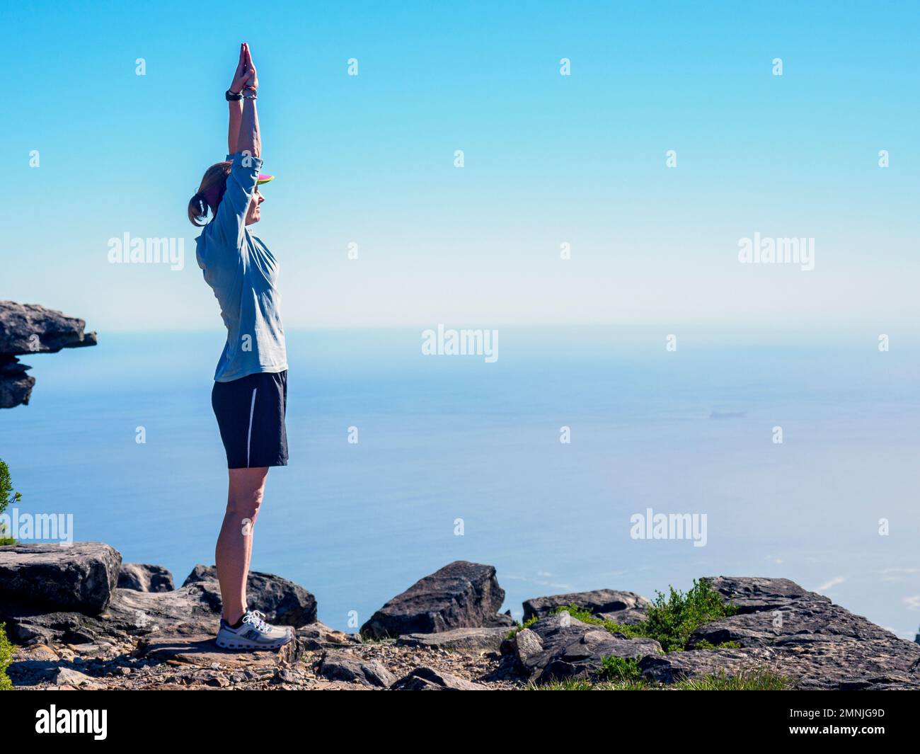 Woman standing on cliff with arms raised Stock Photo