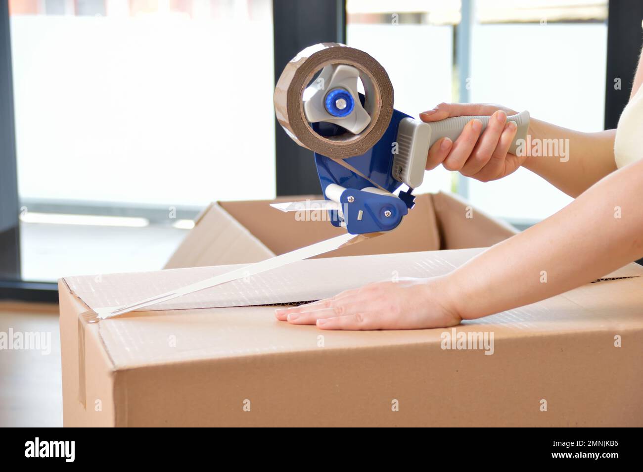 Shot of an unidentifiable young woman closing a cardboard box with tape ...