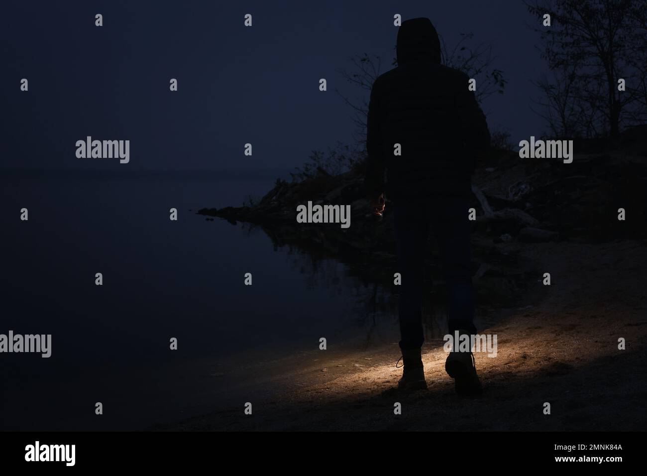 Man with flashlight walking near river in evening Stock Photo