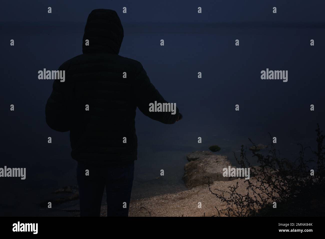 Man with flashlight walking near river in evening Stock Photo