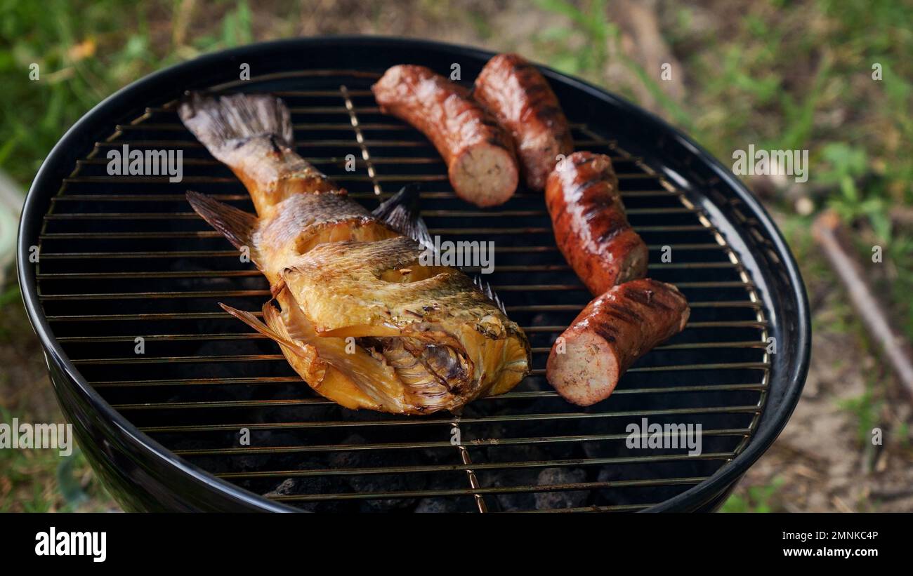 Top view of fresh grilled whole fish, skewer, sausages on round black
