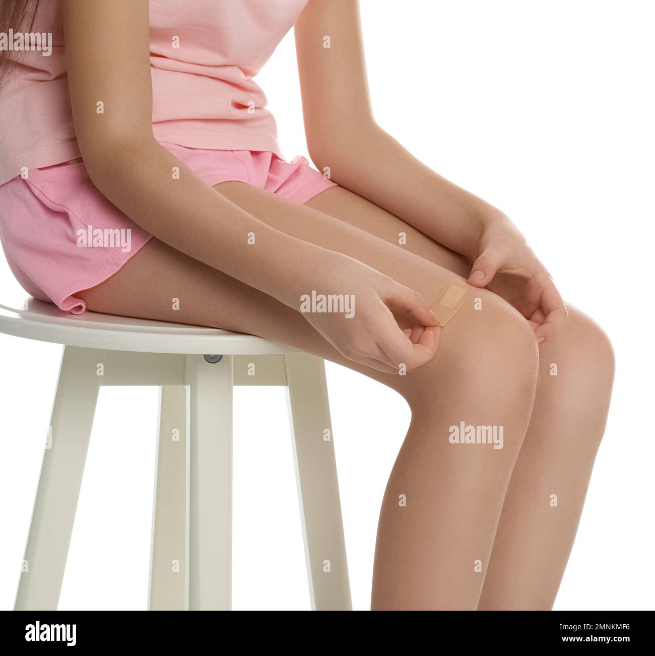 Girl putting sticking plaster onto leg on white background, closeup