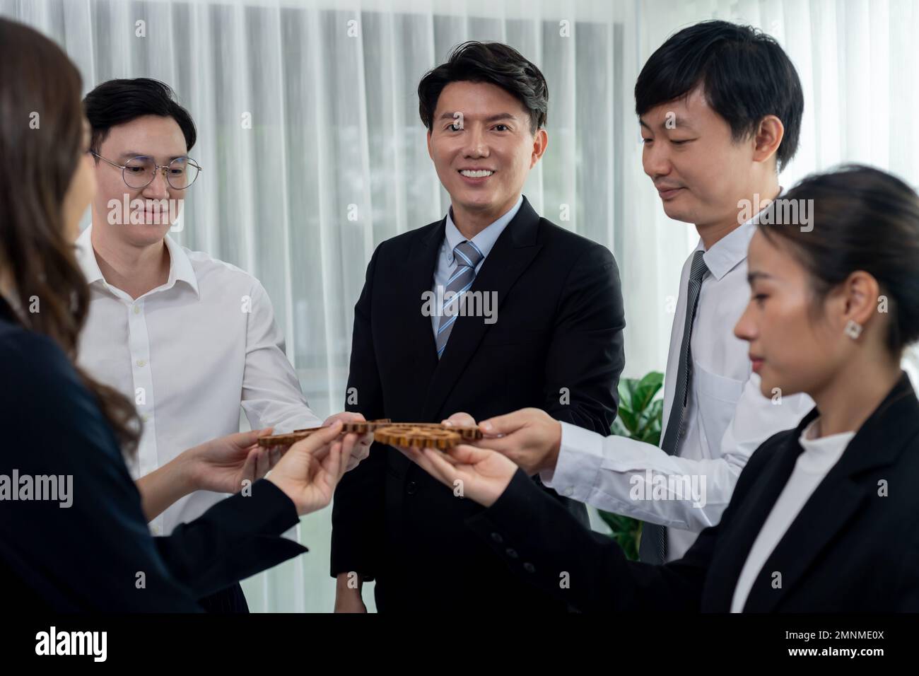 Closeup hand holding wooden gear by businesspeople wearing suit for harmony synergy in office workplace concept. Group of people hand making chain of Stock Photo
