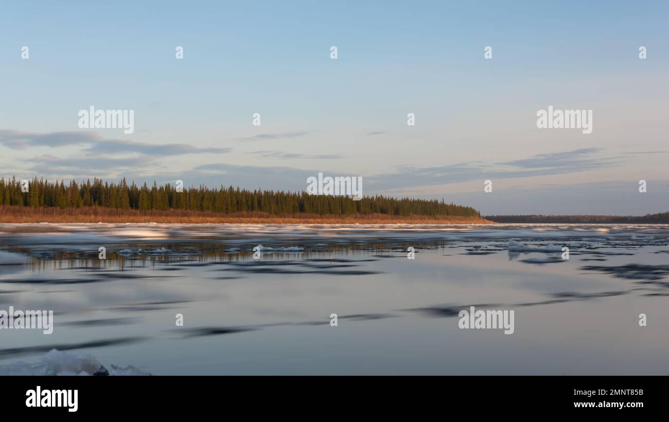 The movement of the flow of water with ice on the ice drift of the northern Vilyui River in Yakutia against the backdrop of the forest. Long exposure. Stock Photo