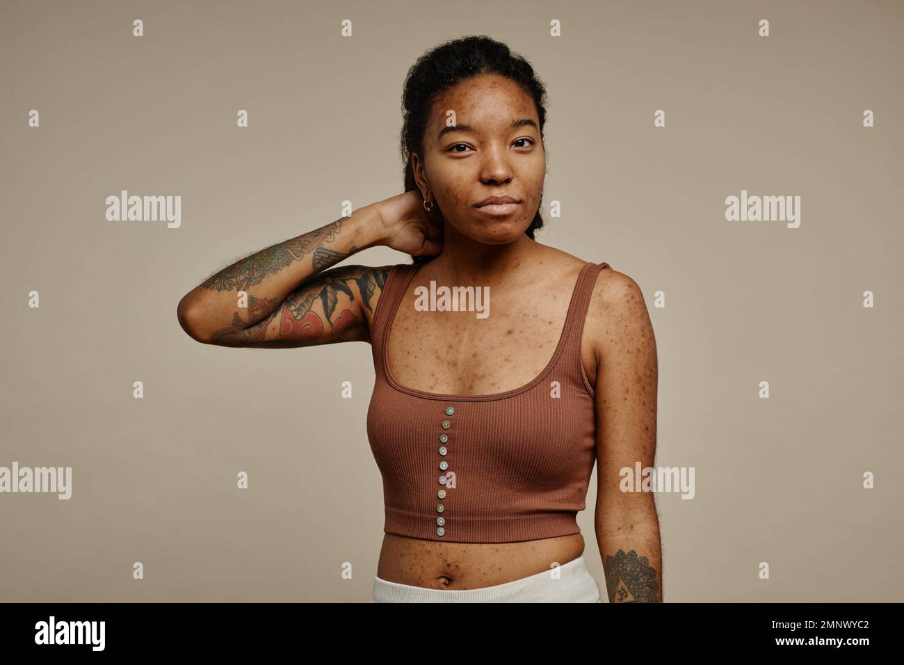 Minimal waist up portrait of ethnic young woman with tattoos looking at camera focus on real skin texture Stock Photo
