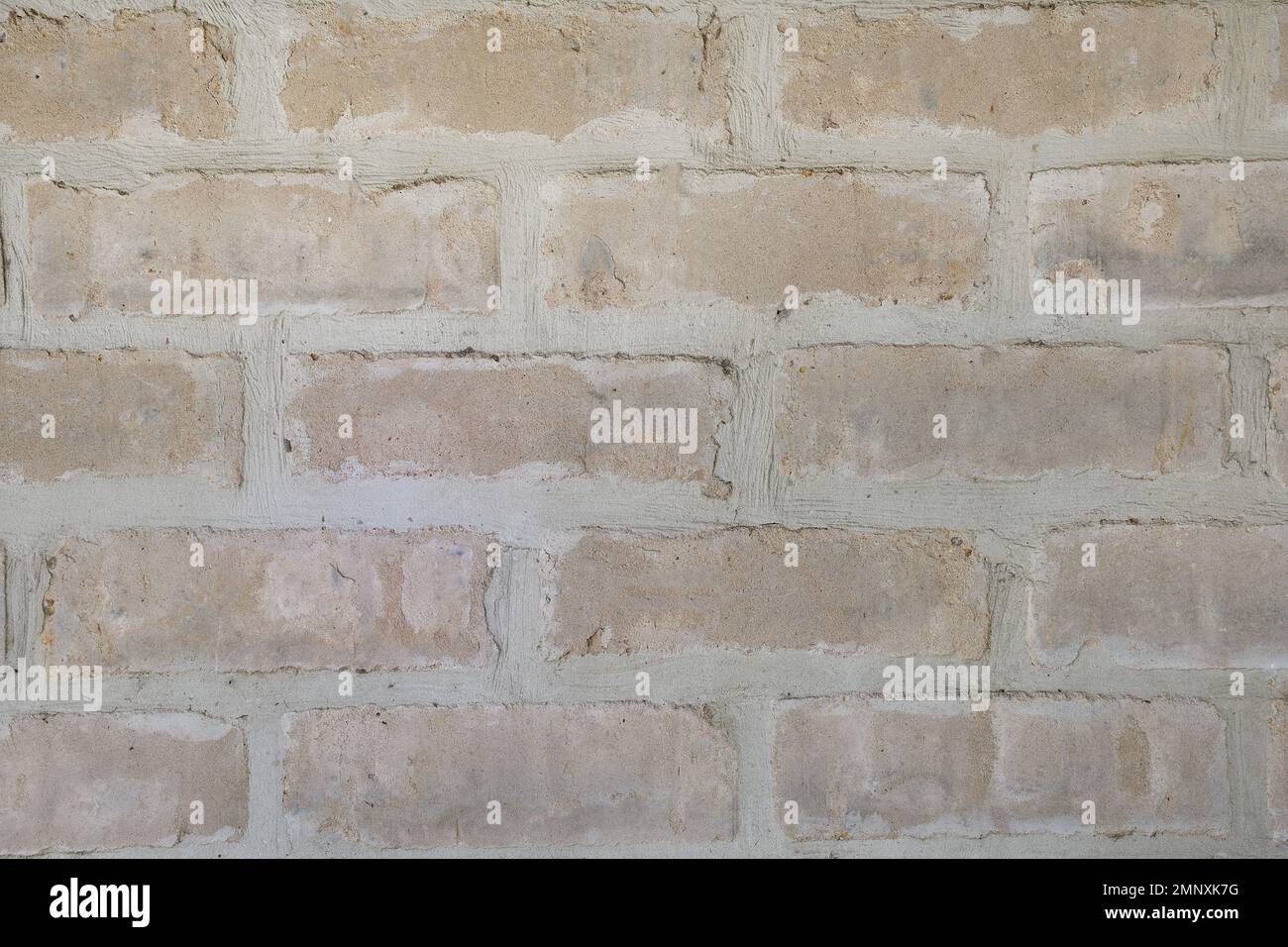 A close-up view of a section of warm, pinkish coloured, coarse, rustic, sandstone looking house bricks with vertical and horizontal joint lines Stock Photo