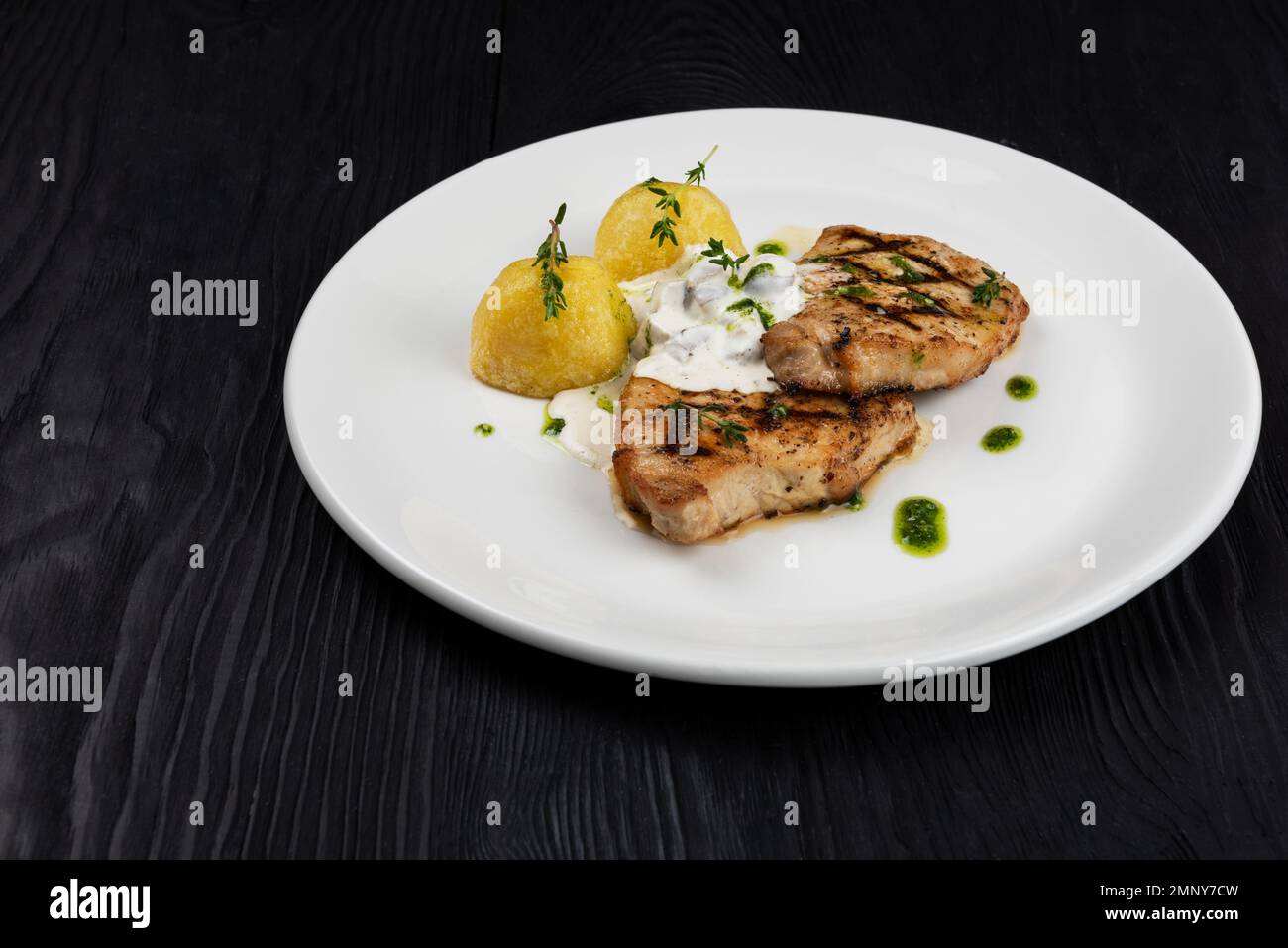 Grilled pork meat with mushroom sauce and potato on white plate on wooden black background Stock Photo