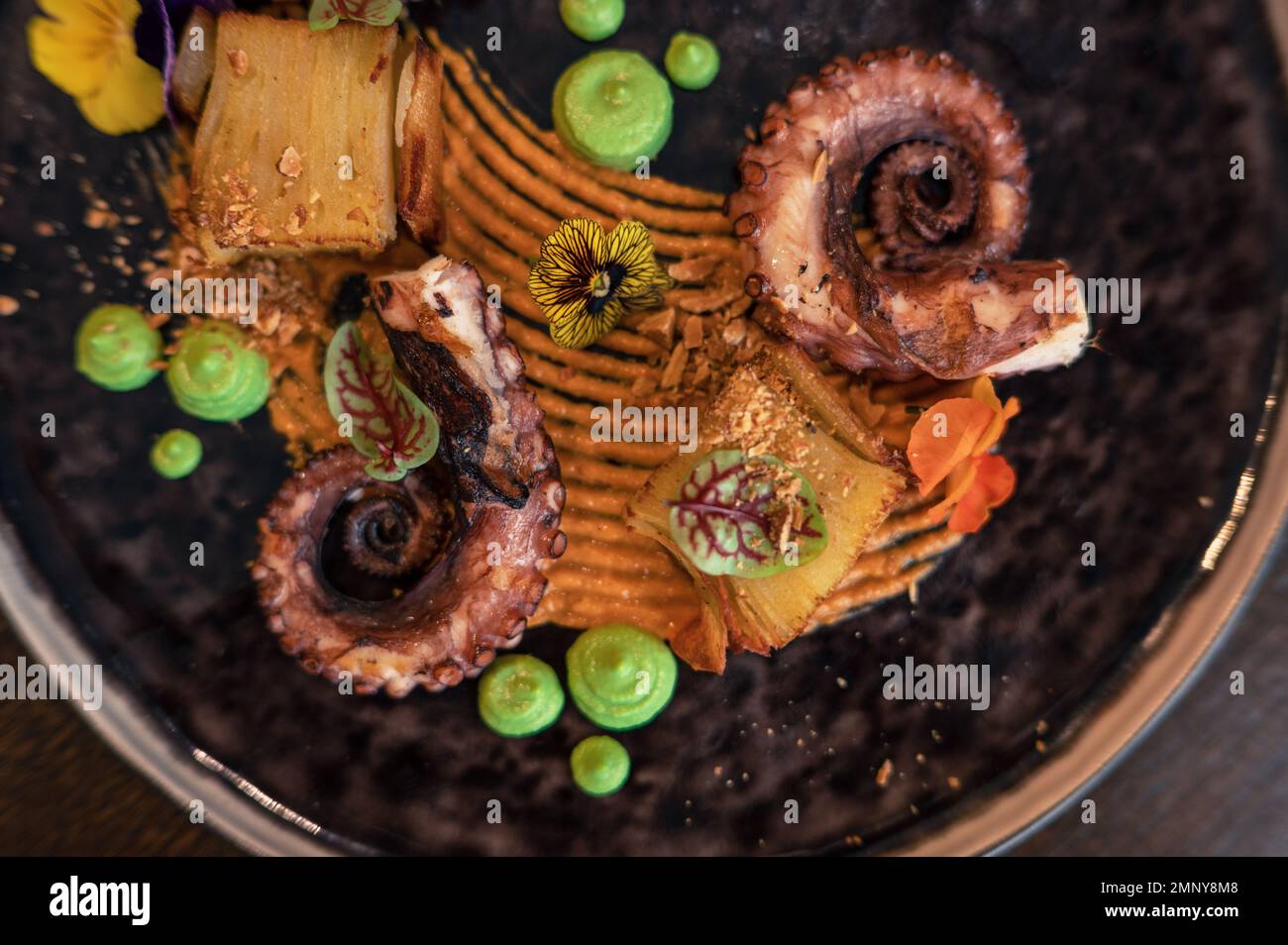 Octopus with potatoes on pea mash decorated with edible flowers Stock Photo