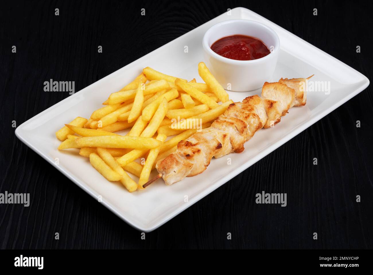 Grilled chicken shashlik meat with fried potatoes on white plate on black wooden background Stock Photo